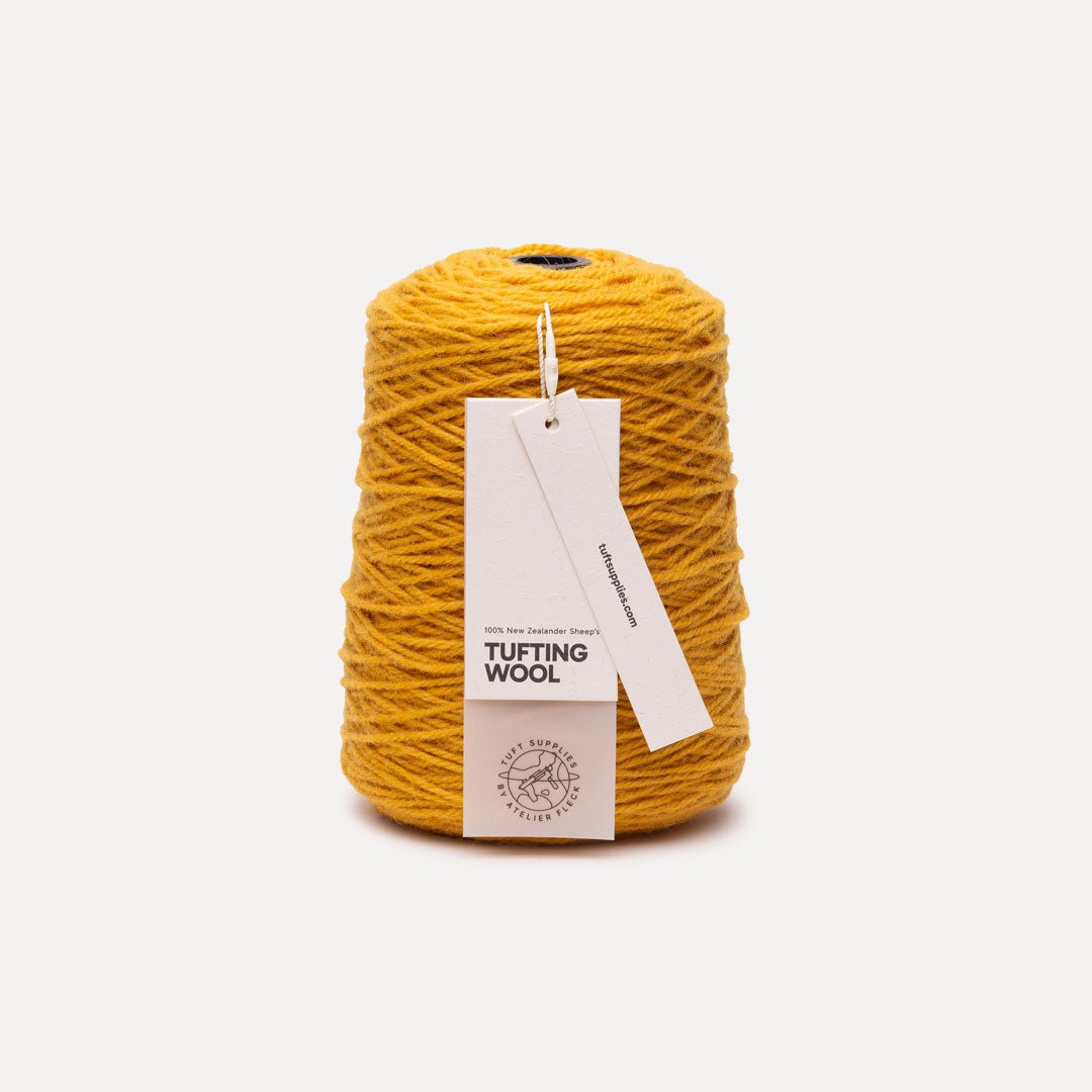 A cone of mustard yellow tufting wool yarn with a white paper hangtag, set against a clean off-white background.