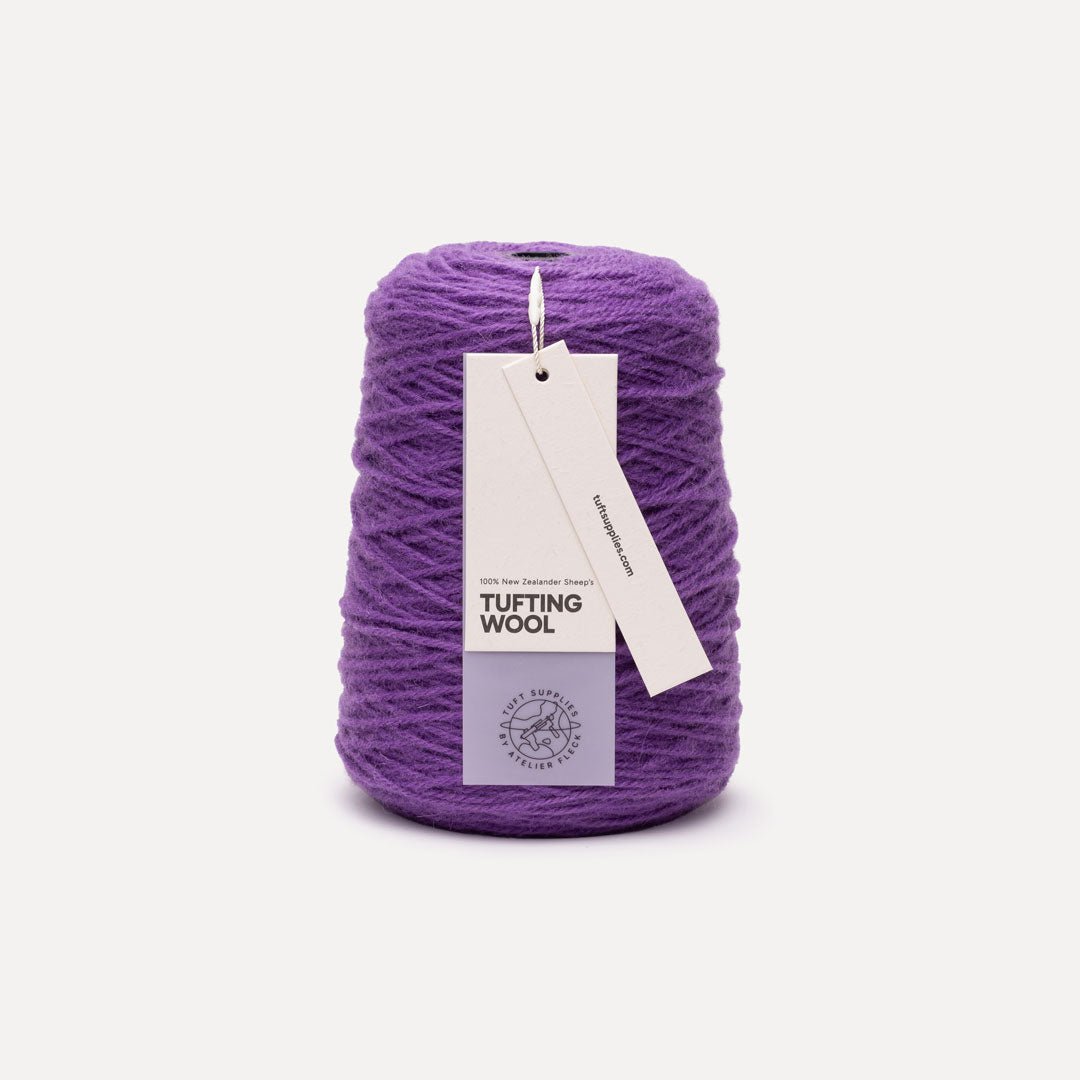 A cone of purple tufting wool yarn with two paper tags attached, photographed on a clean, light off-white background.