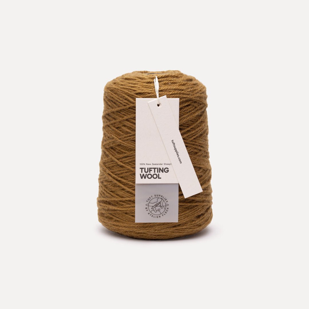 A cone of brown tufting wool yarn with a white paper hangtag, photographed on a clean, light gray background.
