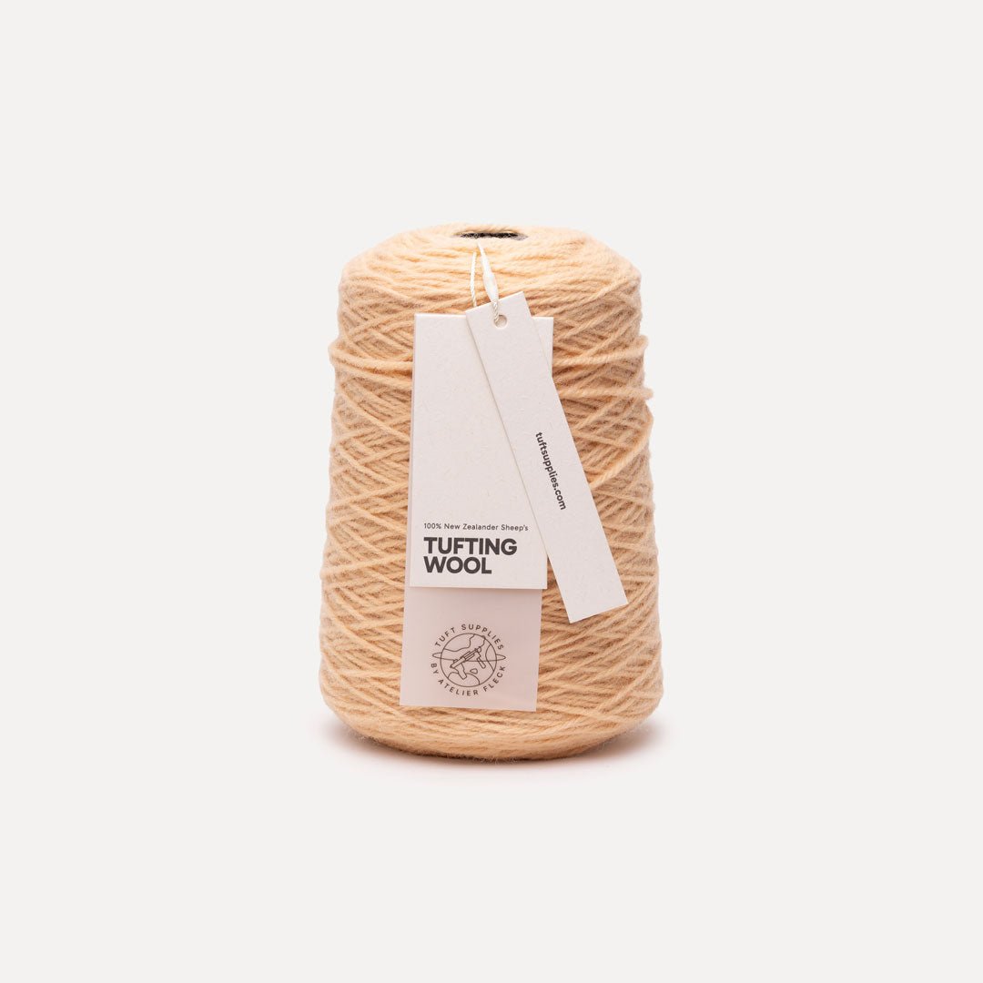 A cone of beige tufting wool yarn with a white paper hangtag, photographed on a clean, light off-white background.