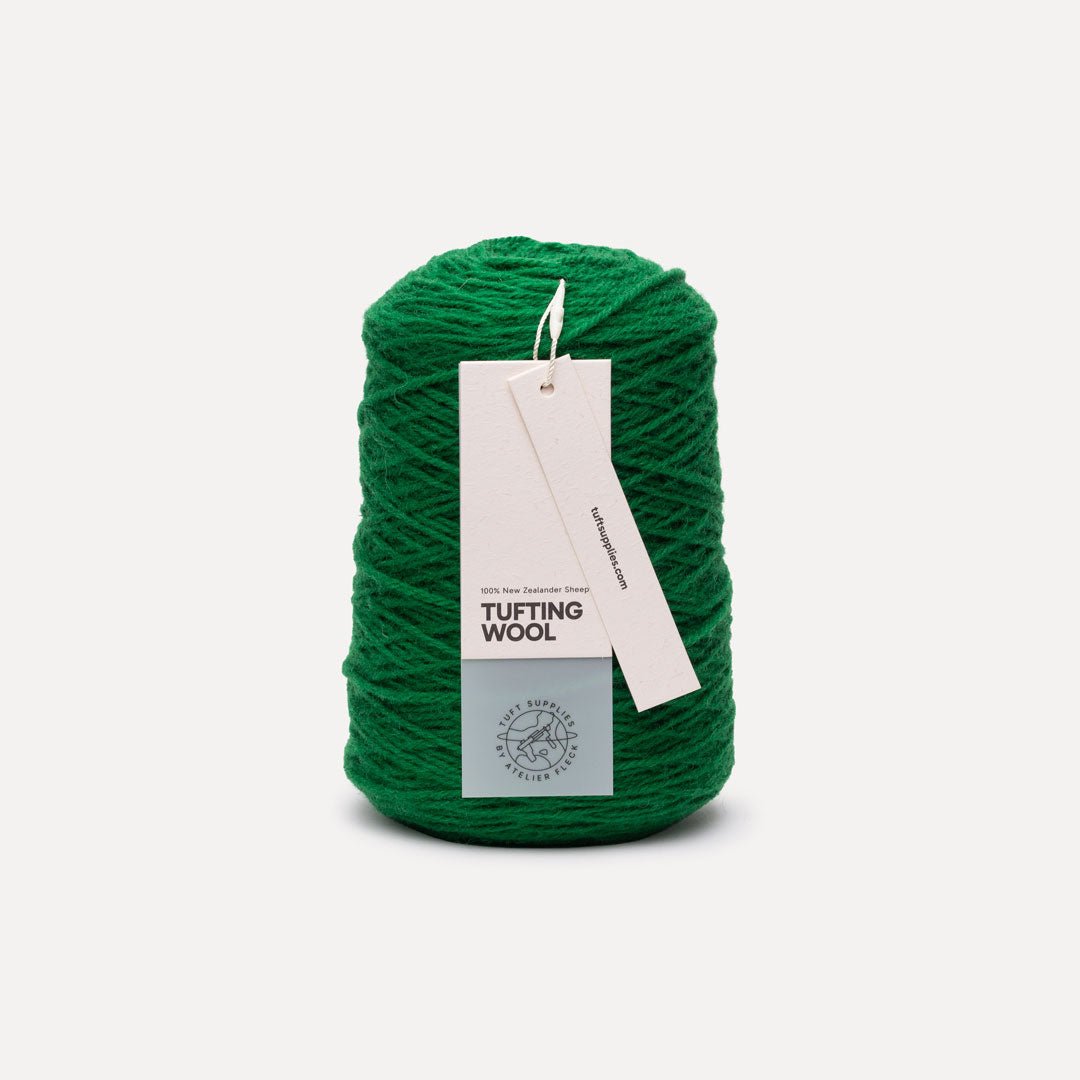 A single cone of bright green tufting wool yarn with a white paper hangtag, photographed on a clean, light gray background.