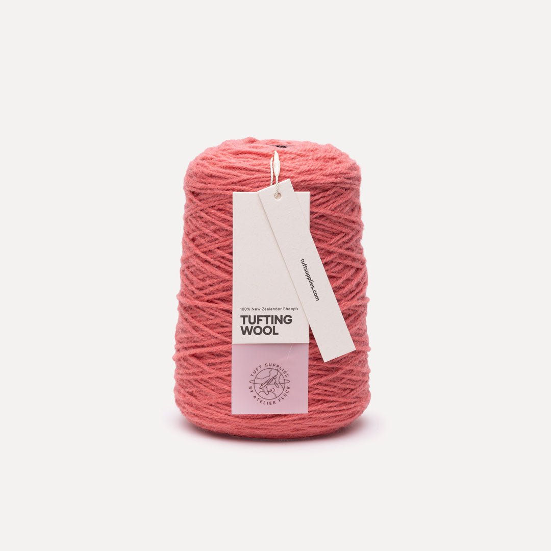 A spool of dusty pink tufting wool yarn with a white paper hangtag, set against a clean off-white background.