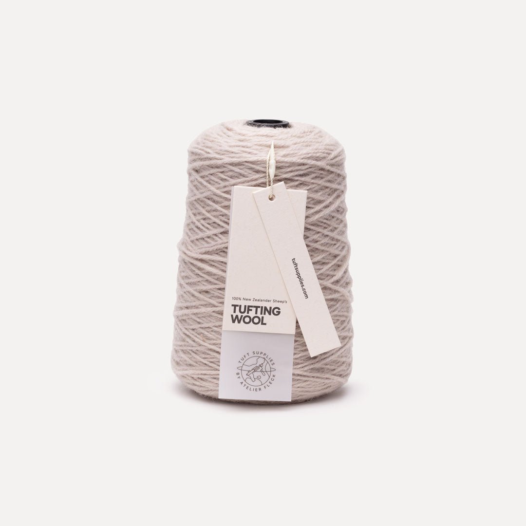 A cone spool of light beige tufting wool yarn with two paper tags, one reading 'TUFTING WOOL', on a clean off-white background.