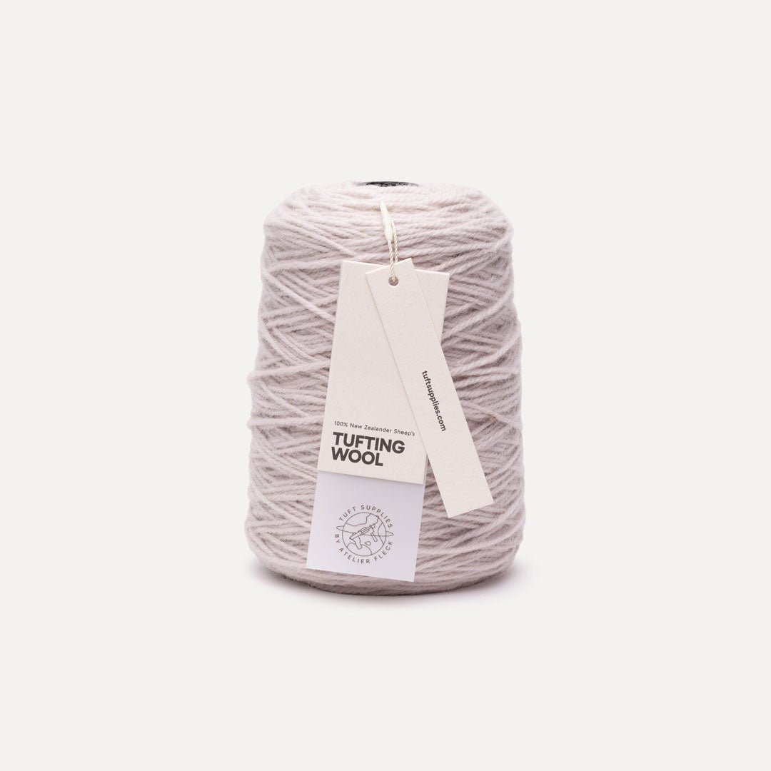 A cone of light gray tufting wool yarn with two paper tags attached, set against a solid off-white background.
