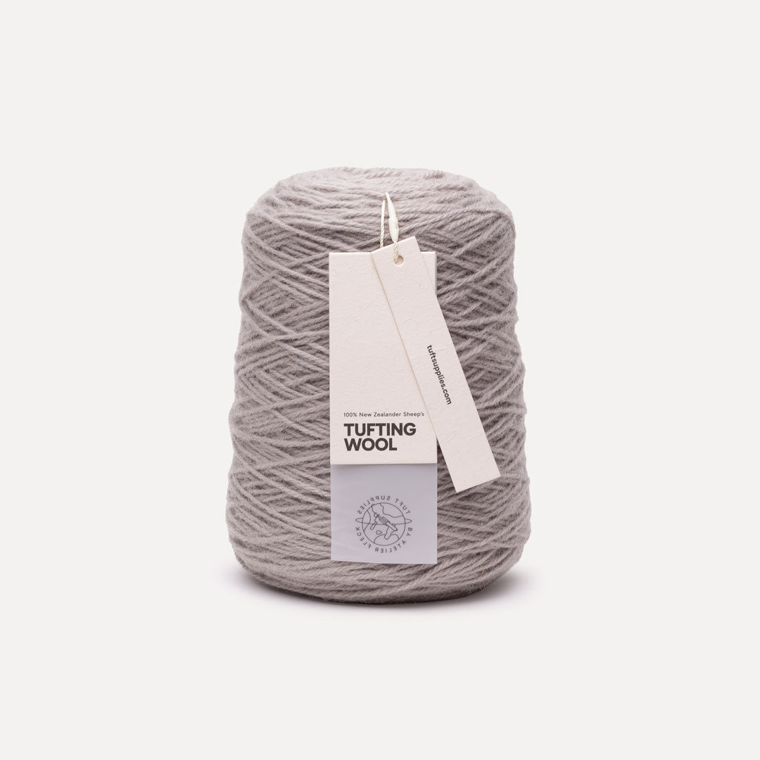 A spool of light gray tufting wool yarn with two paper tags attached, photographed against a clean, off-white background.