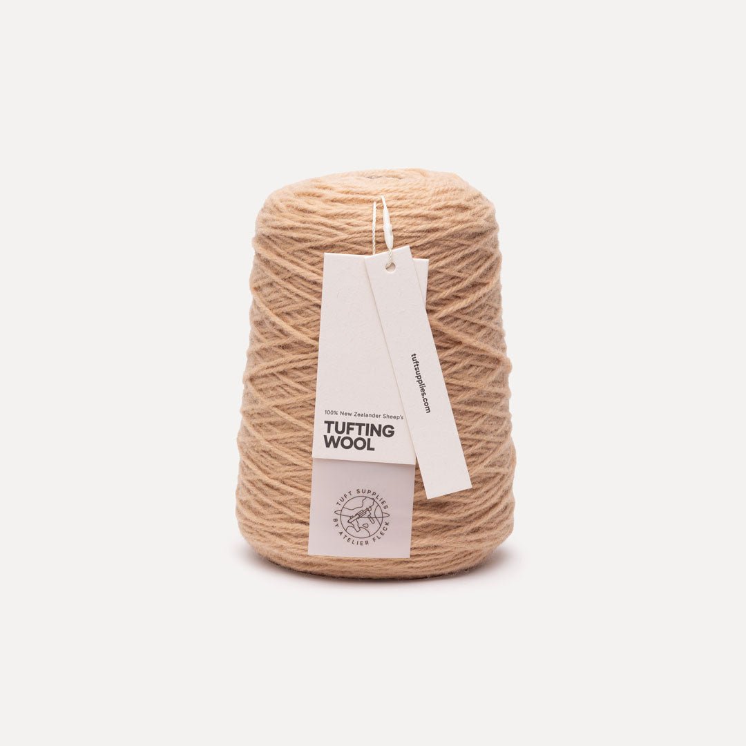 A cone of beige tufting wool yarn with two paper tags attached, photographed against a clean, light off-white background.