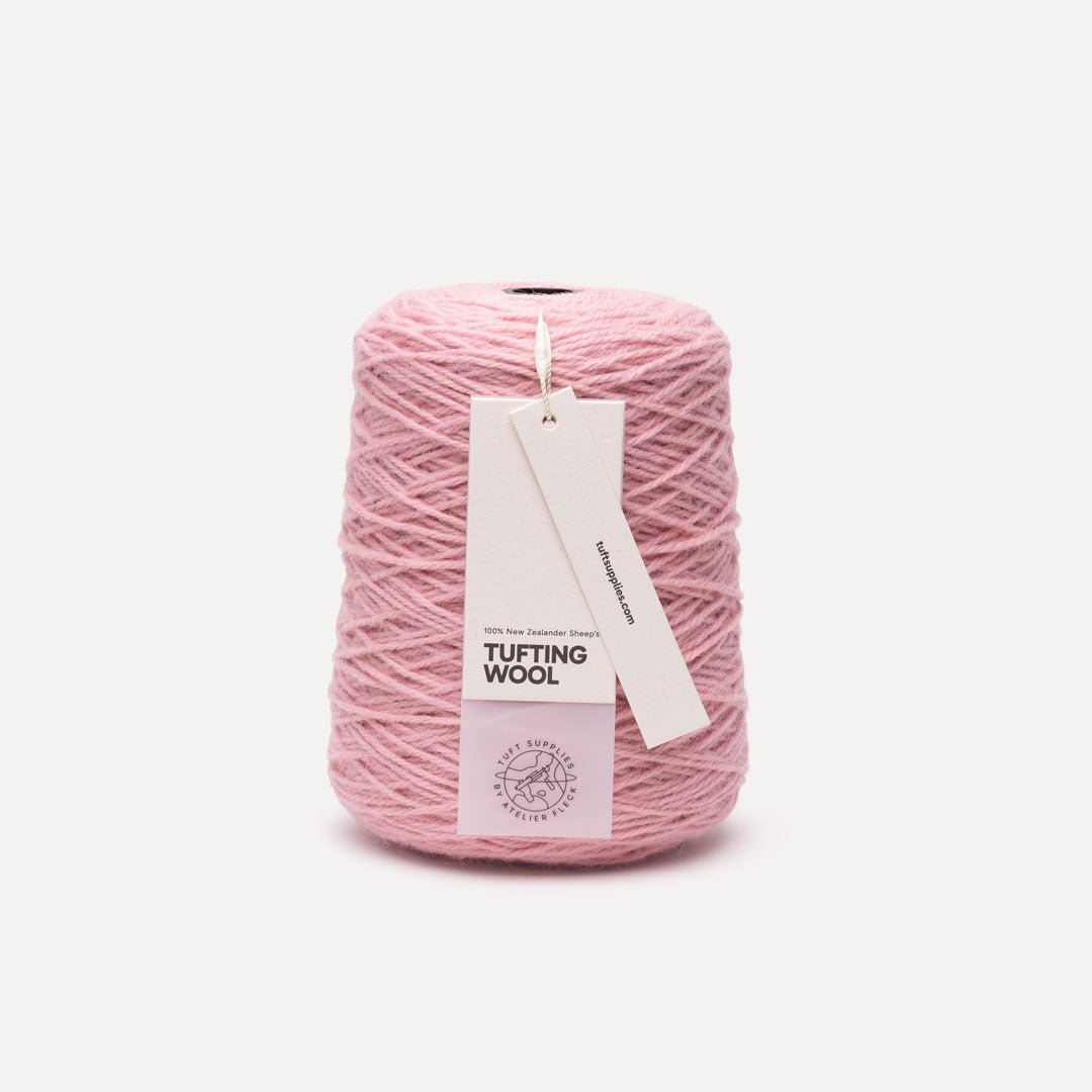 A cone of dusty pink tufting wool yarn with two paper tags attached, one reading 'TUFTING WOOL' and the other 'Tuft Supplies', set against a plain off-white background.