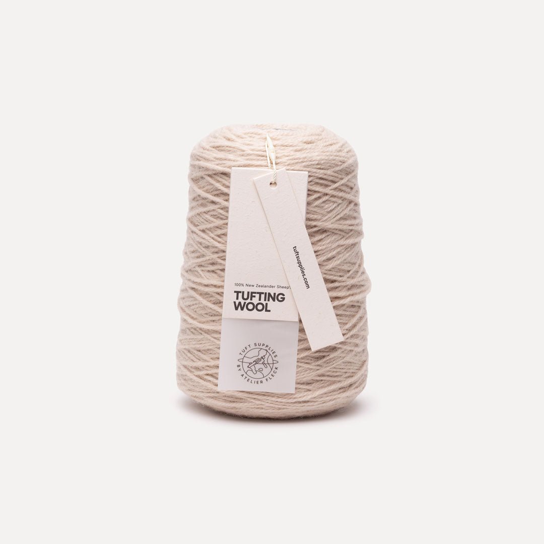 A cone of beige tufting wool yarn with a white paper hangtag, photographed against a clean, solid off-white background.