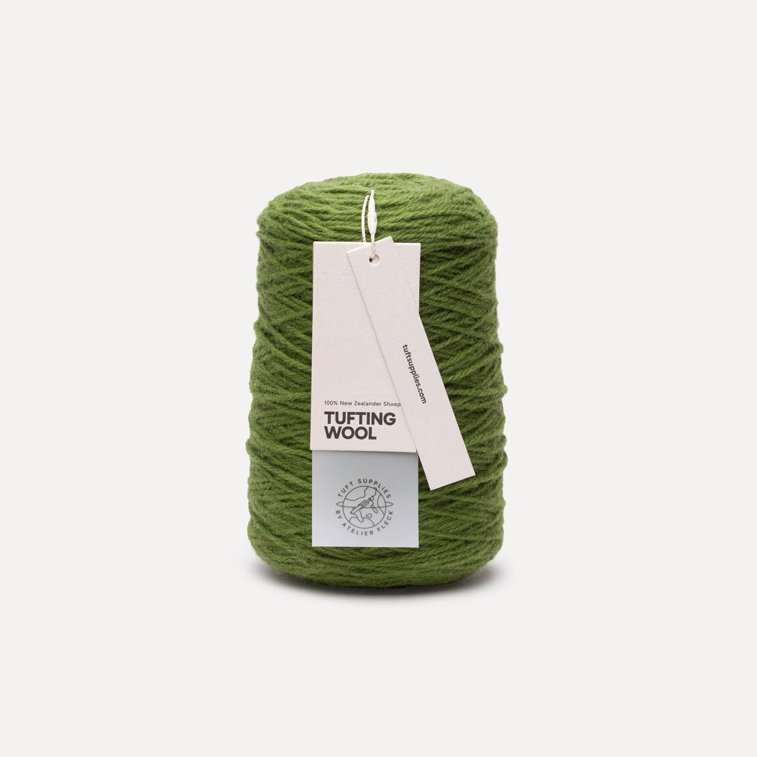 A spool of olive green tufting wool yarn with a white paper hangtag, set against a plain light gray background.