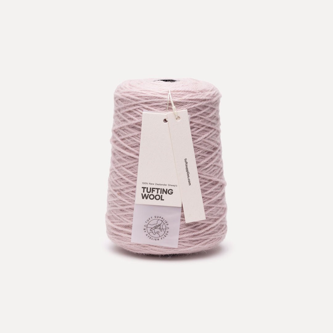 A cone of light pink tufting wool yarn with a white paper hangtag, set against a clean off-white background.