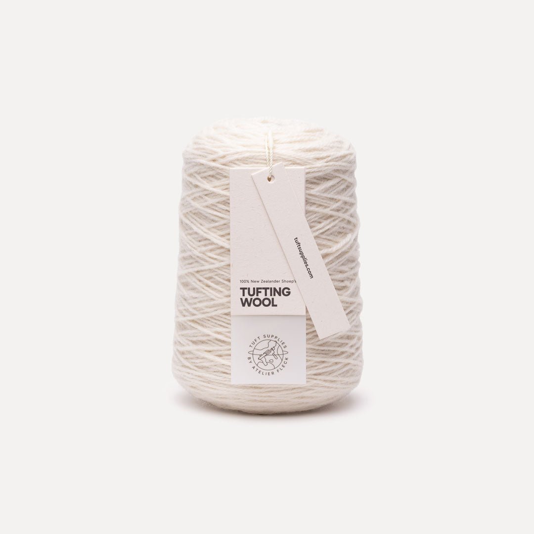 A cone of off-white tufting wool yarn with a white paper hangtag reading 'TUFTING WOOL' and 'The Wool Society', photographed on a clean, light gray background.