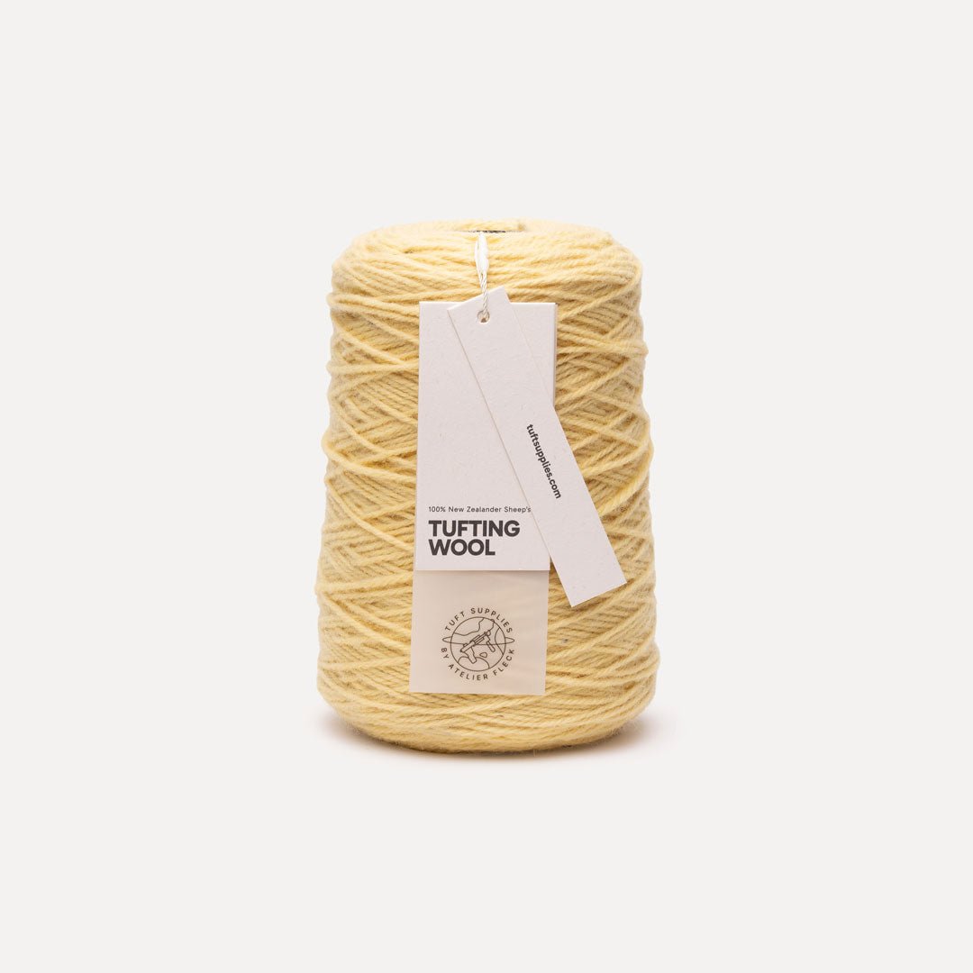 A spool of light yellow tufting wool yarn with a white paper hangtag, photographed against a clean, light gray background.