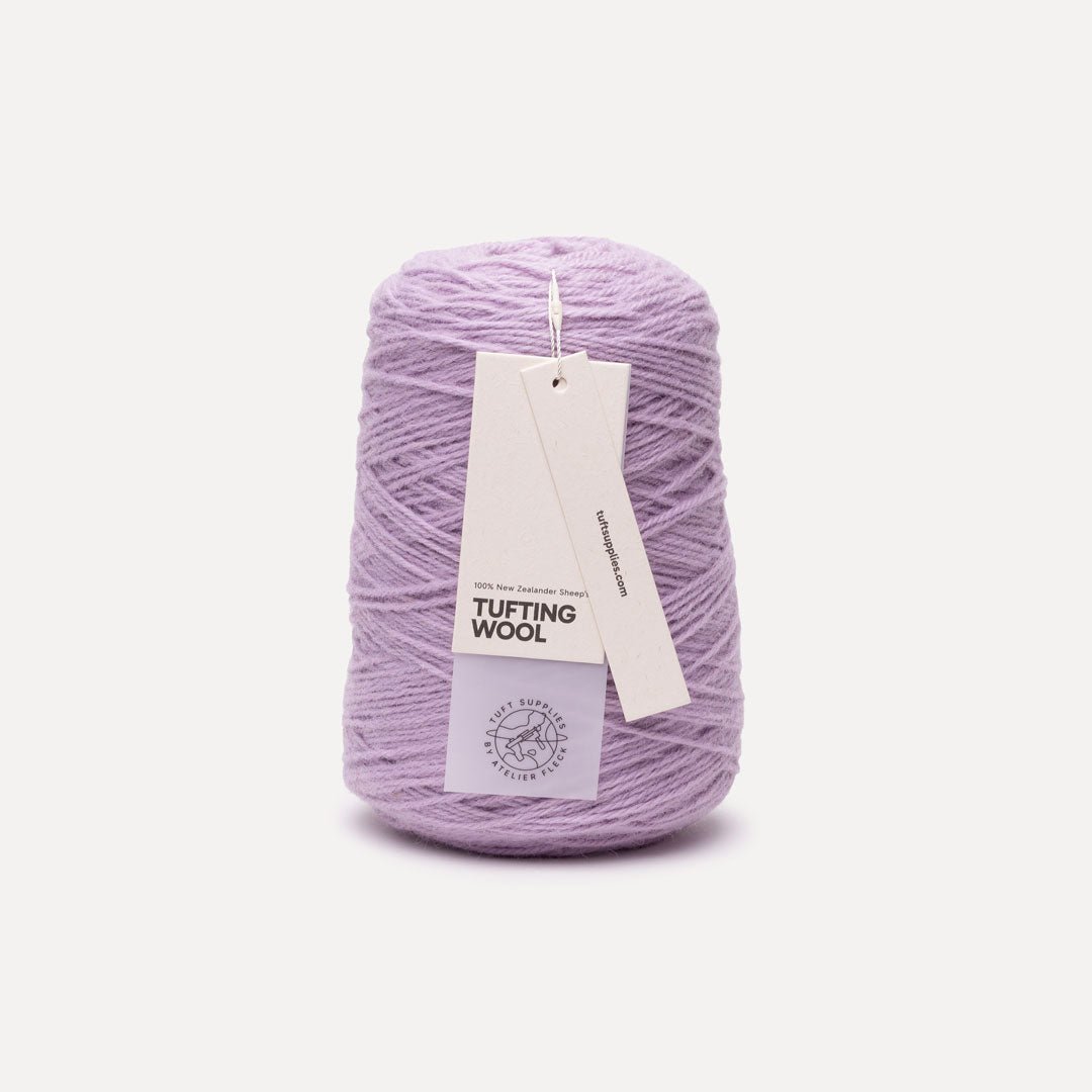 A cone of light purple/lavender tufting wool yarn with two paper tags attached, set against a plain off-white background.
