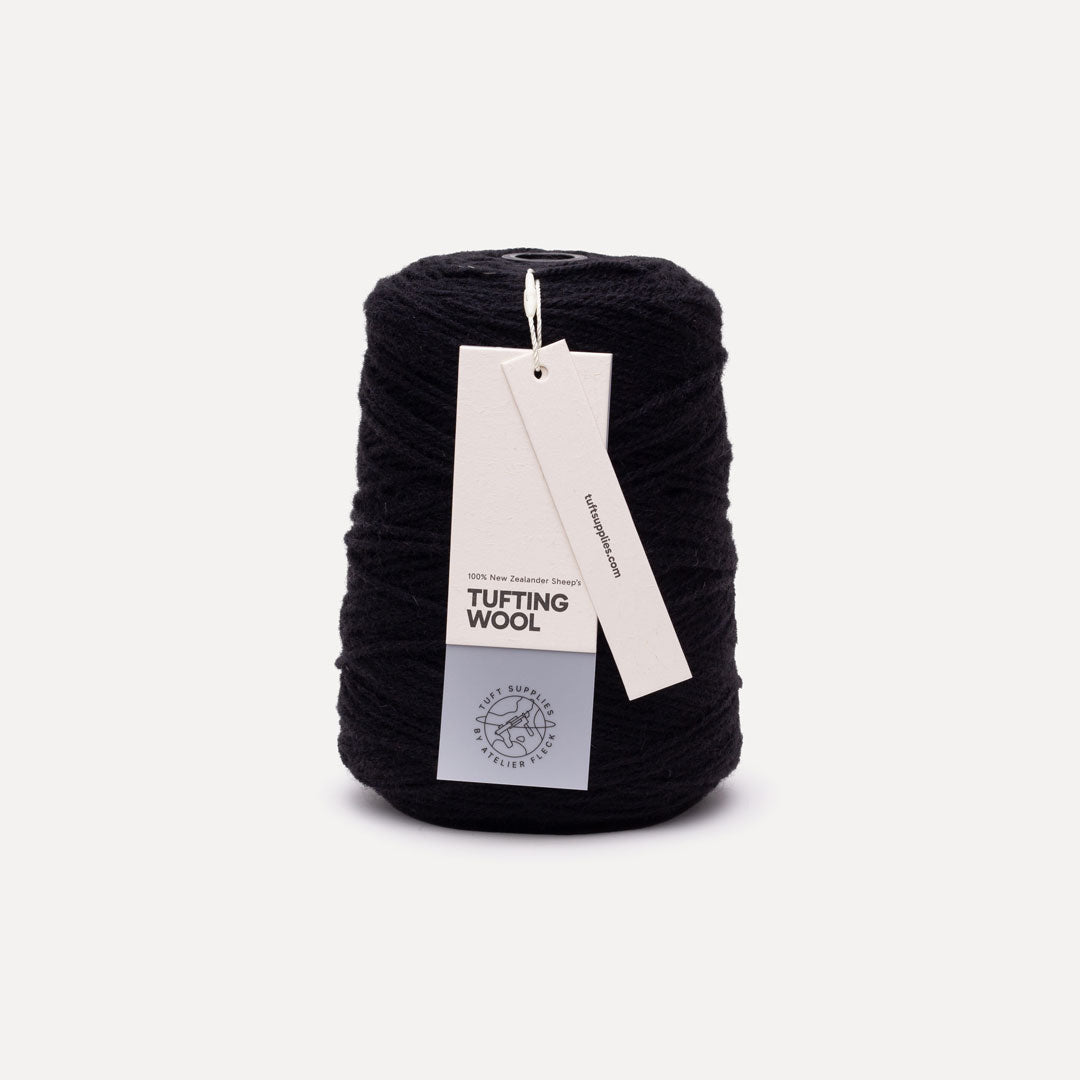 A black spool of tufting wool yarn with white paper labels attached, photographed against a clean, light off-white background.