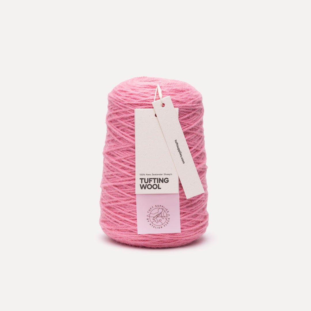 A cone of pink tufting wool yarn with a white paper hangtag, photographed against a clean, light off-white background.