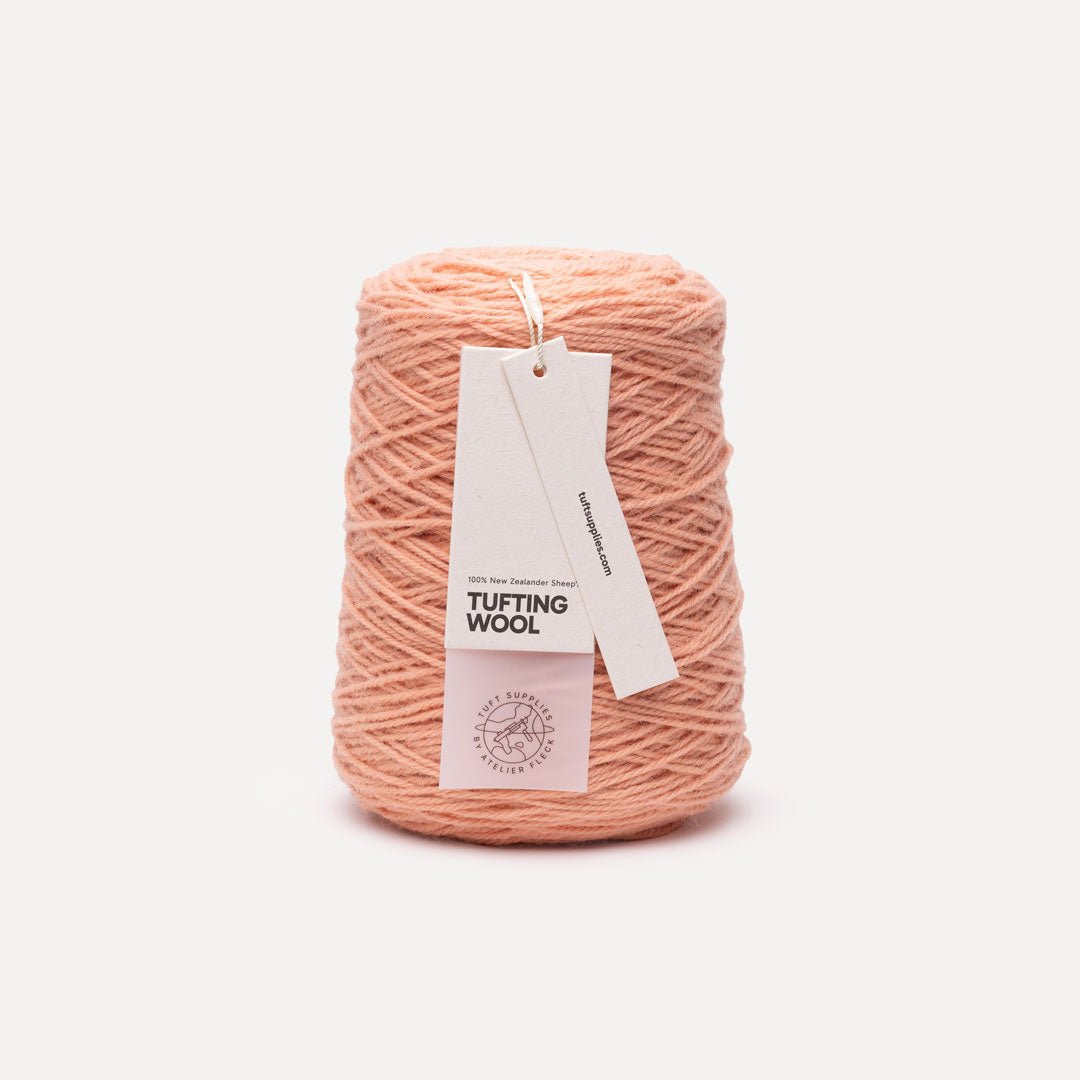 A cone of peach-colored tufting wool yarn with a white paper hangtag, set against a clean, light off-white background.