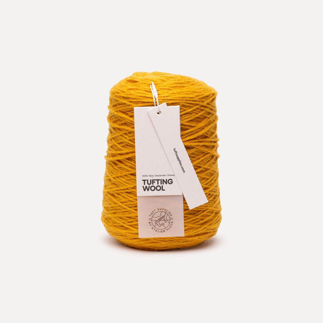A cone of mustard yellow tufting wool yarn with a white paper hangtag, photographed against a clean, light off-white background.