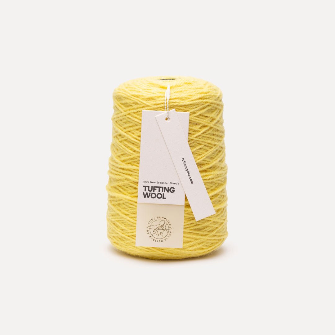 A cone of yellow tufting wool yarn with two white paper tags attached, set against a clean, light gray background.