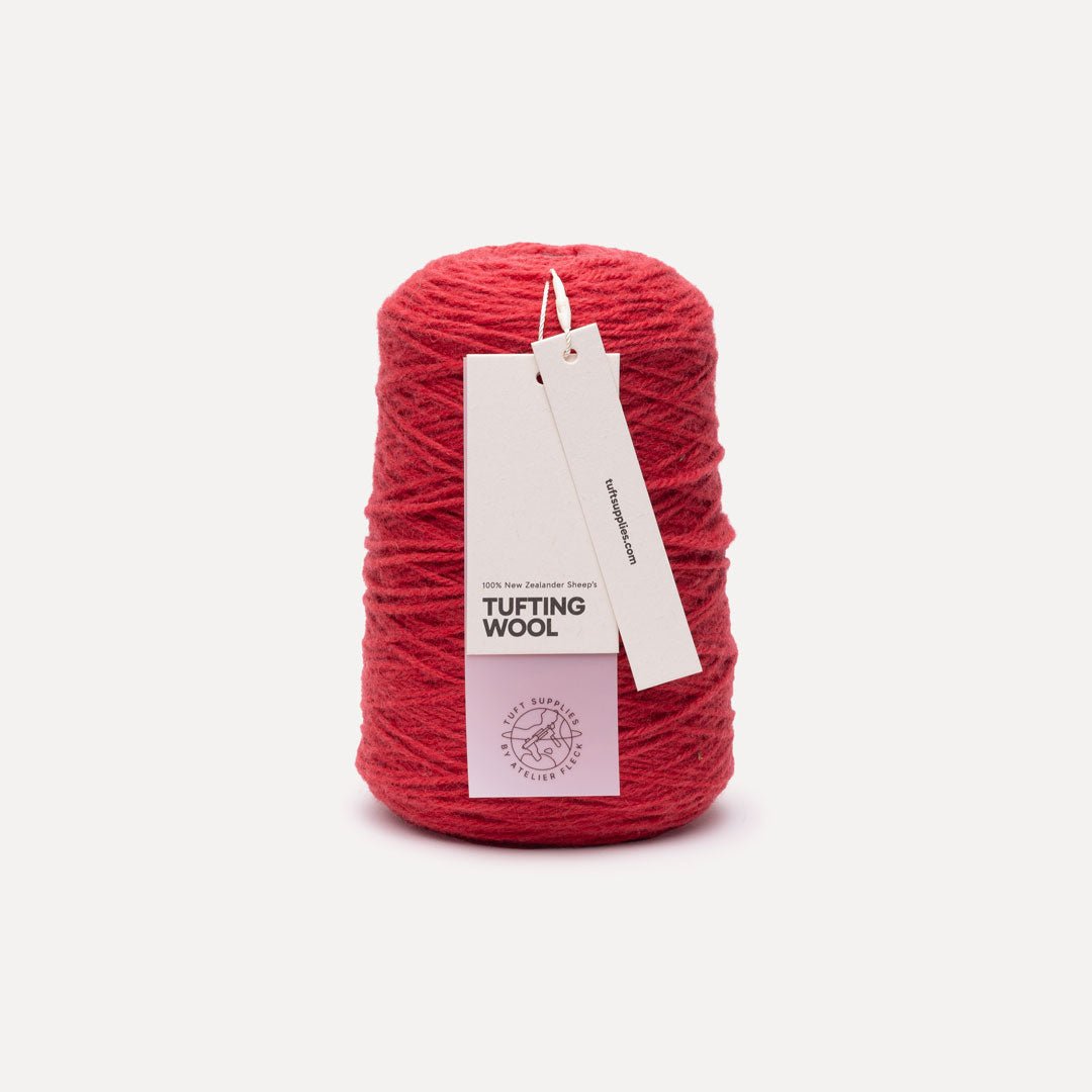 A skein of vibrant red tufting wool yarn with a white paper hangtag, set against a clean, light off-white background.