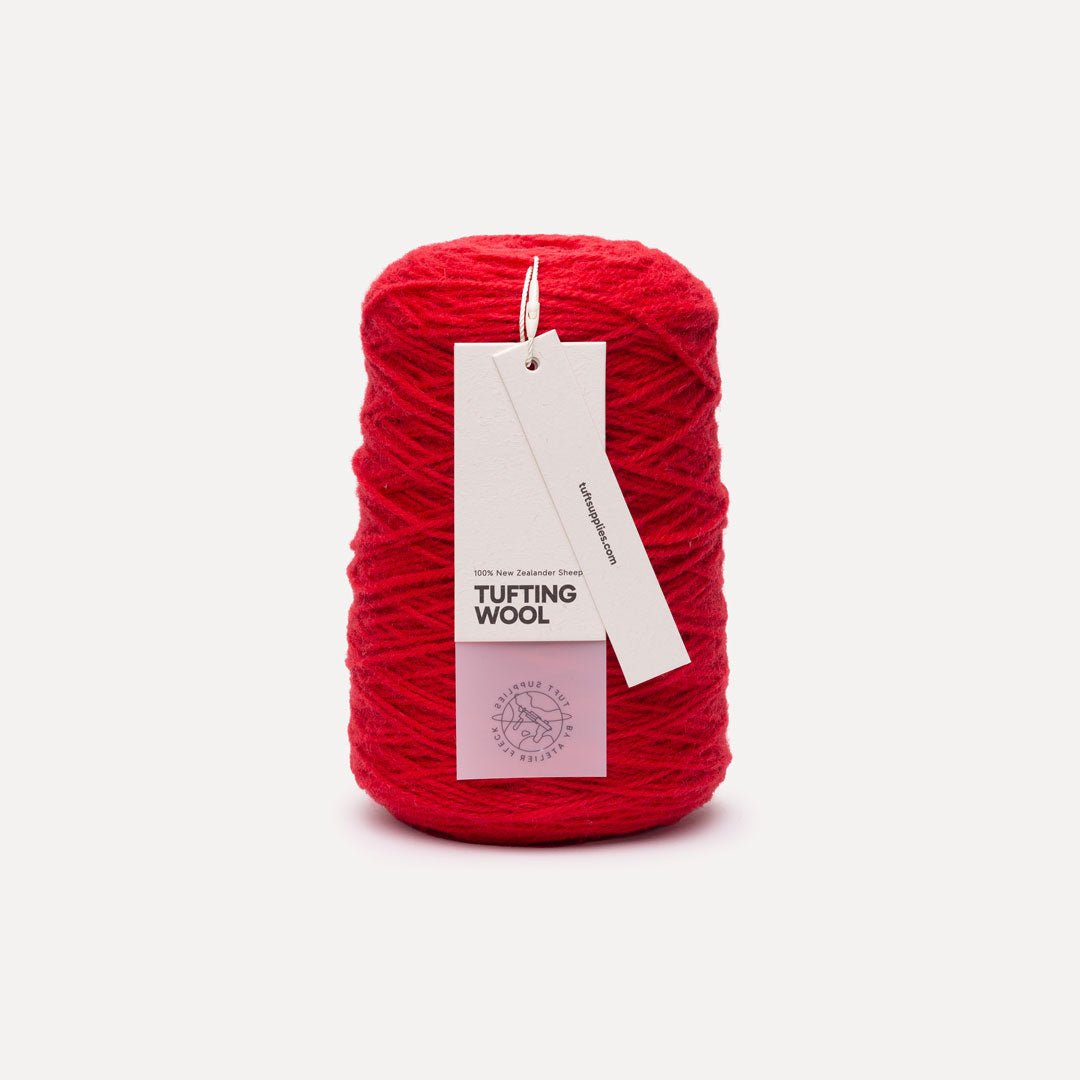 A skein of vibrant red tufting wool yarn with a white paper hangtag, set against a clean, light off-white background.