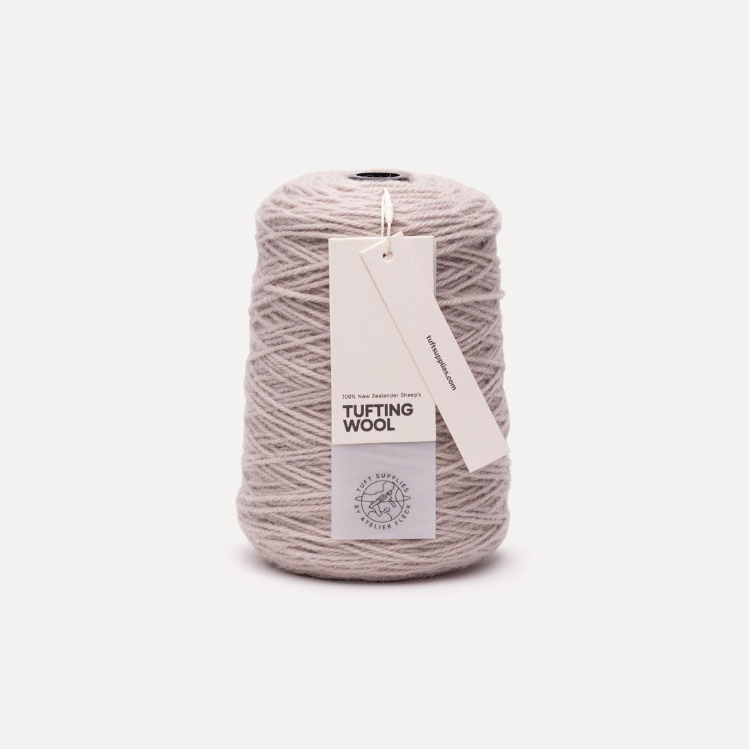 A spool of light taupe gray tufting wool yarn with a white paper hangtag, photographed on a clean, solid off-white background.