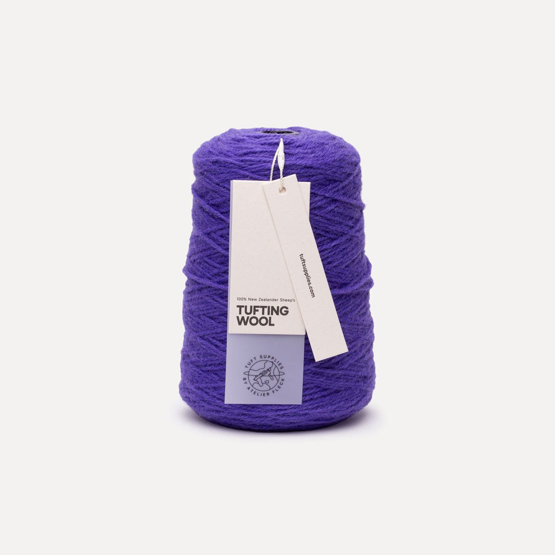 A cone of purple tufting wool yarn with a white paper hangtag, photographed on a clean, light off-white background.
