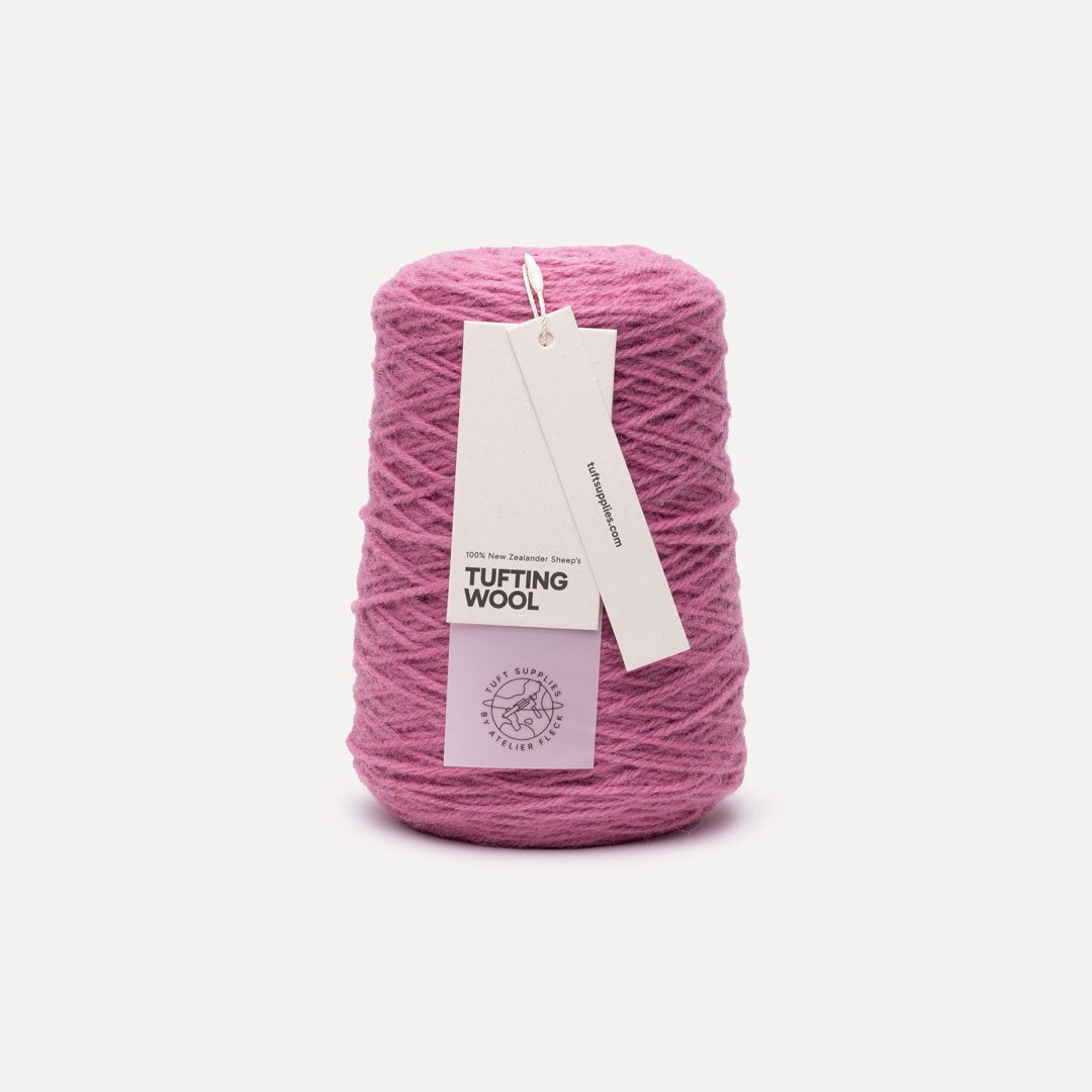 A spool of dusty pink tufting wool yarn with a white paper hangtag, set against a clean off-white background.