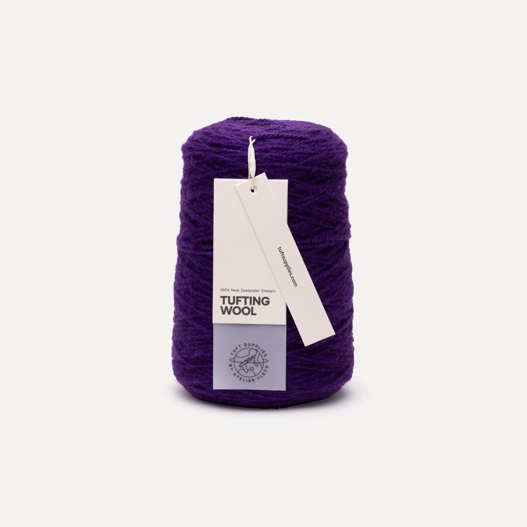 A single skein of deep purple tufting wool yarn with a white paper hangtag, photographed against a clean, light off-white background.