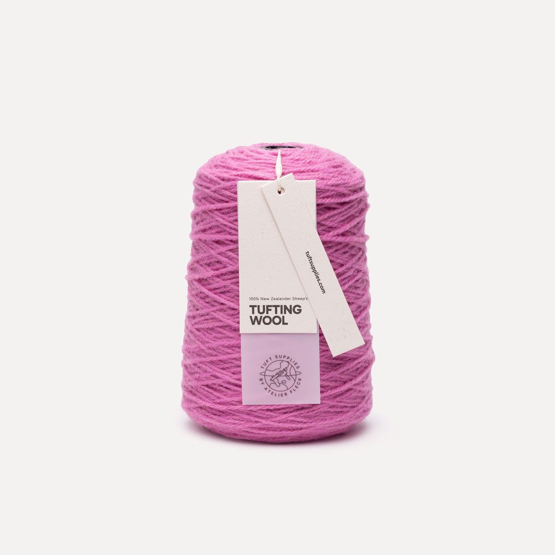 A cone of bright pink tufting wool yarn with a white paper hangtag reading 'TUFTING WOOL' and 'Tuft Supplies', photographed on a clean off-white background.