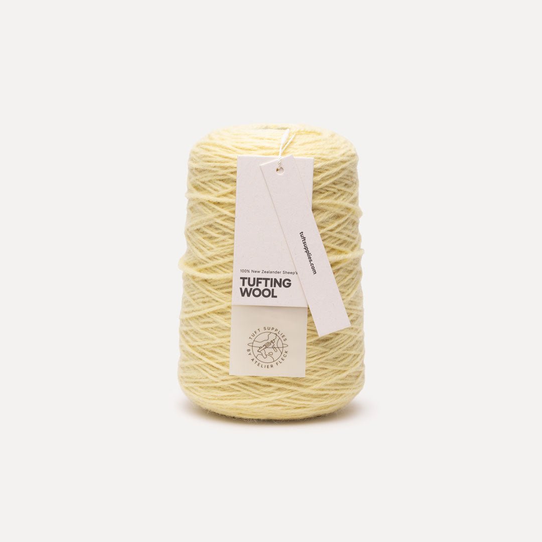 A spool of pale yellow tufting wool yarn with a white paper hangtag, photographed against a clean, light gray background.
