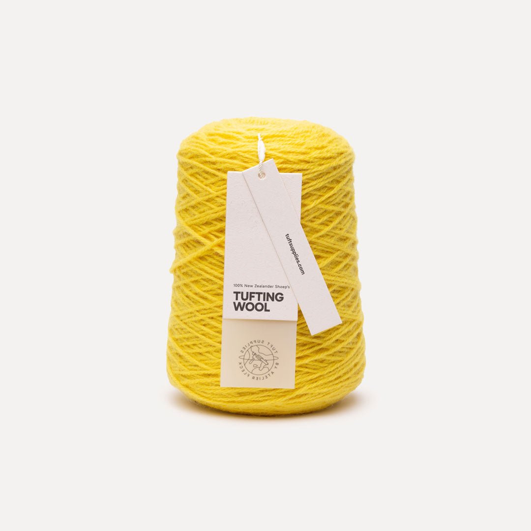 A cone of bright yellow tufting wool yarn with a white paper hangtag, photographed against a clean, light gray background.