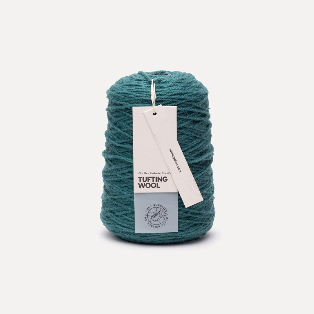 A skein of teal tufting wool yarn with a white paper hangtag, photographed on a clean, light off-white background.