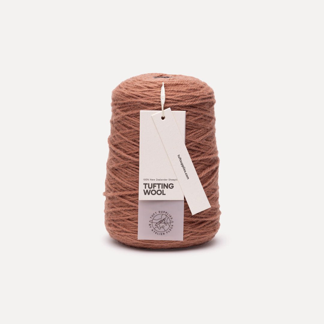 A cone of dusty rose brown tufting wool yarn with a white paper hangtag, set against a clean off-white background.