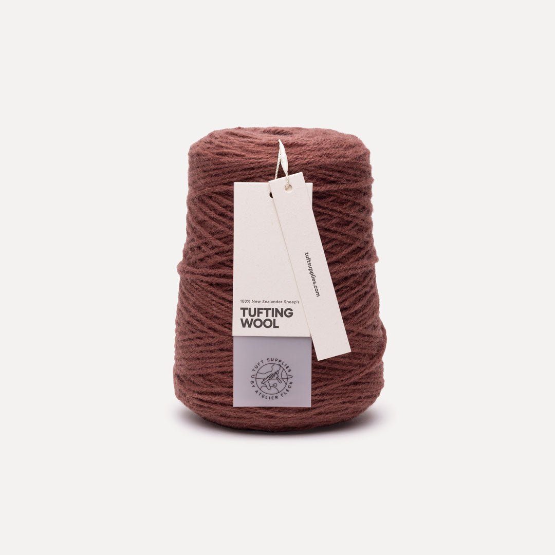 A cone of dusty rose brown tufting wool yarn with a white paper hangtag, set against a clean off-white background.