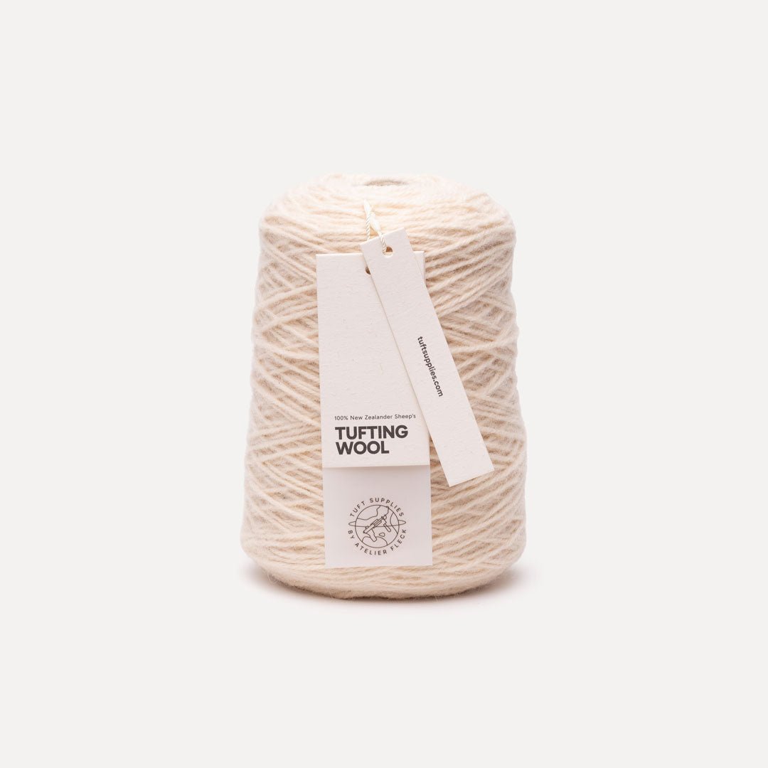 A cone of off-white tufting wool yarn with a white paper hangtag, photographed against a clean, light gray studio background.