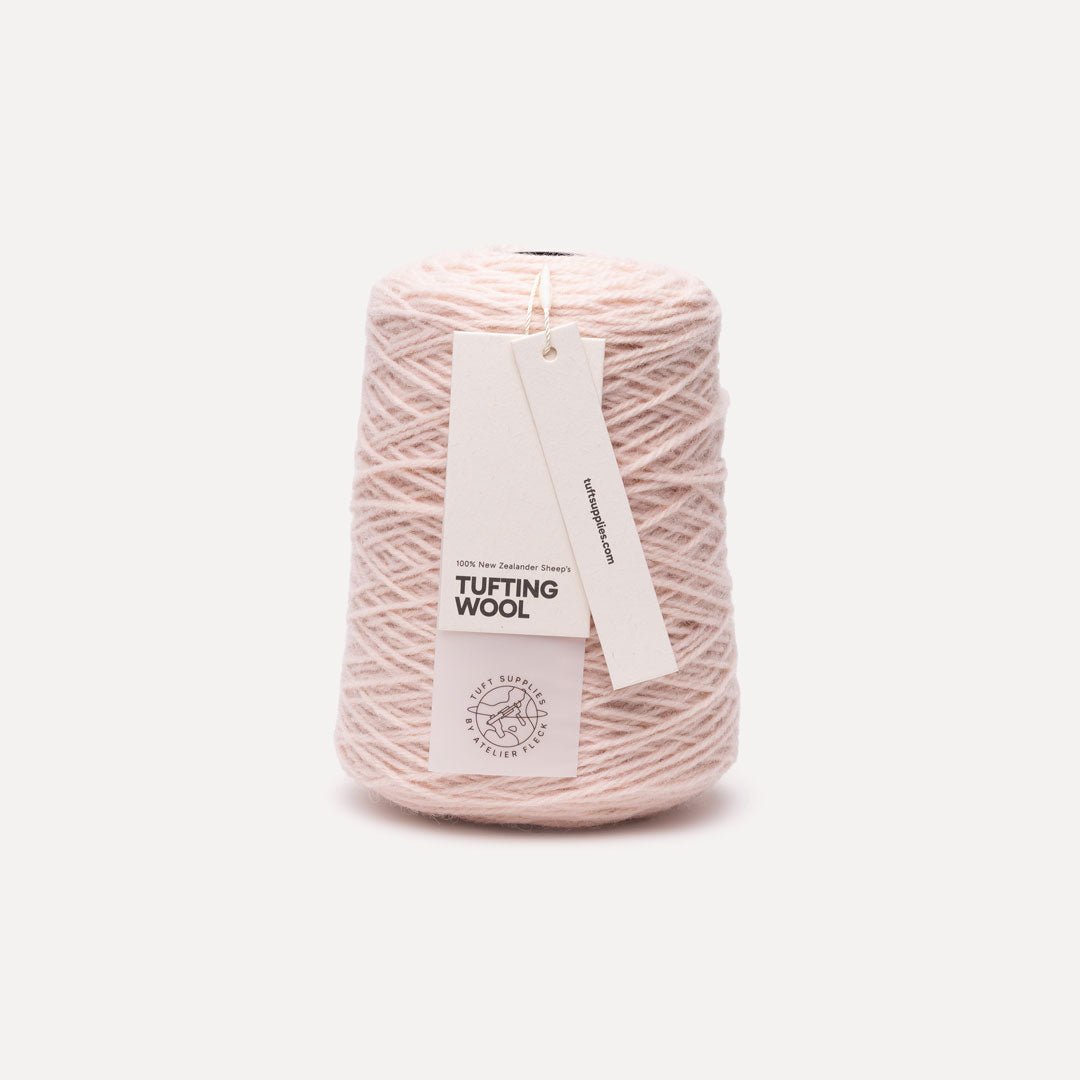 A cone of light pink tufting wool yarn with two paper tags attached, one reading 'TUFTING WOOL' and the other showing the 'tuft supplies' logo, set against a plain off-white background.