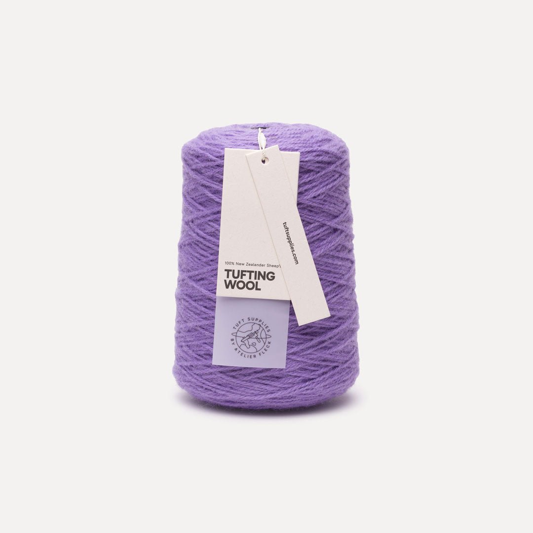 A spool of lavender purple tufting wool yarn with a white paper hangtag, set against a clean off-white background.