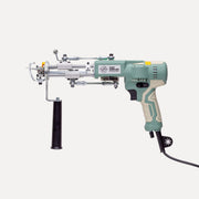 A tufting maschine with a sage green and beige handle, silver metal head, and a black vertical handle attachment, shown against a light gray background.