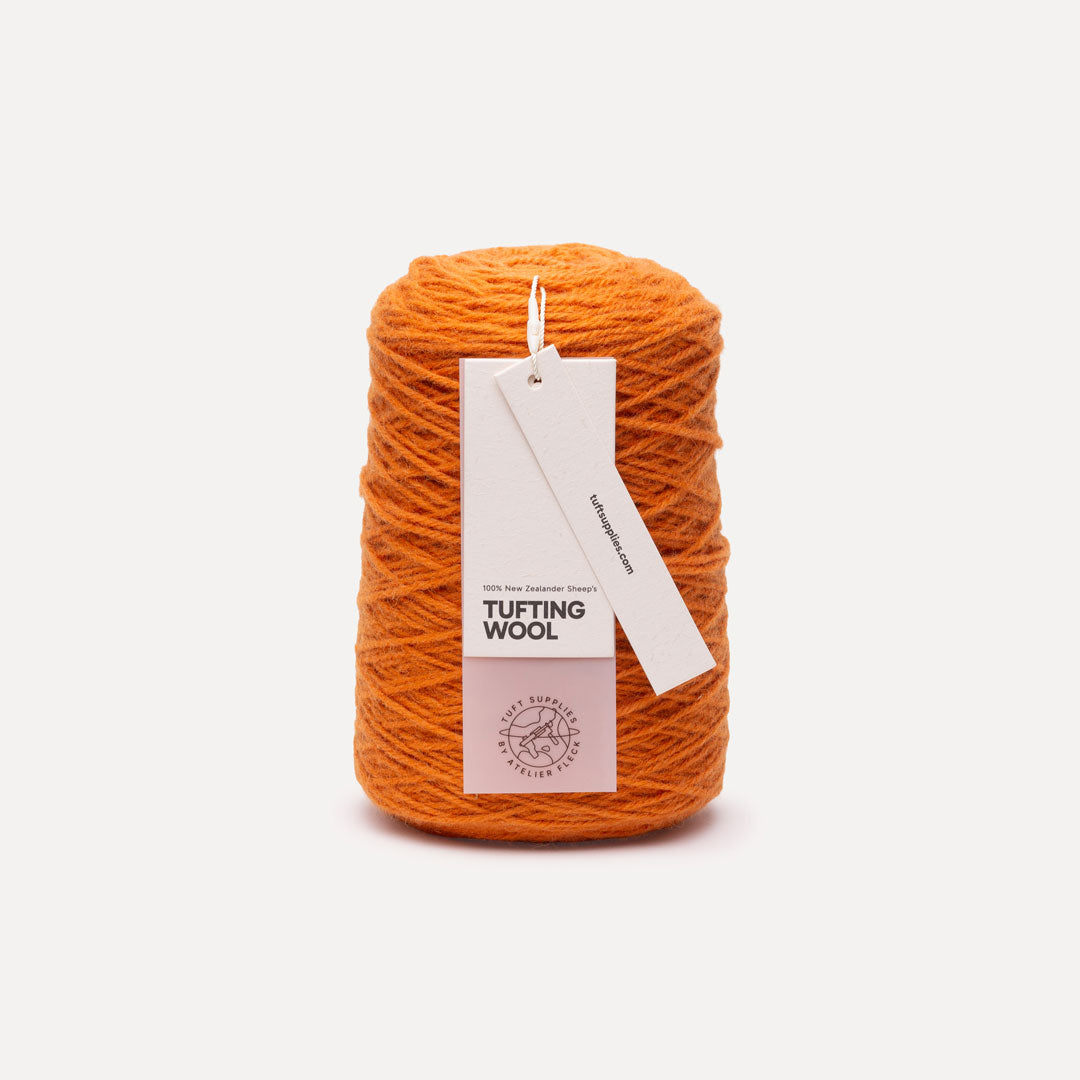A cone of bright orange tufting wool yarn with a white paper hangtag reading 'TUFTING WOOL' and 'Tuft Supplies', photographed on a clean off-white background.