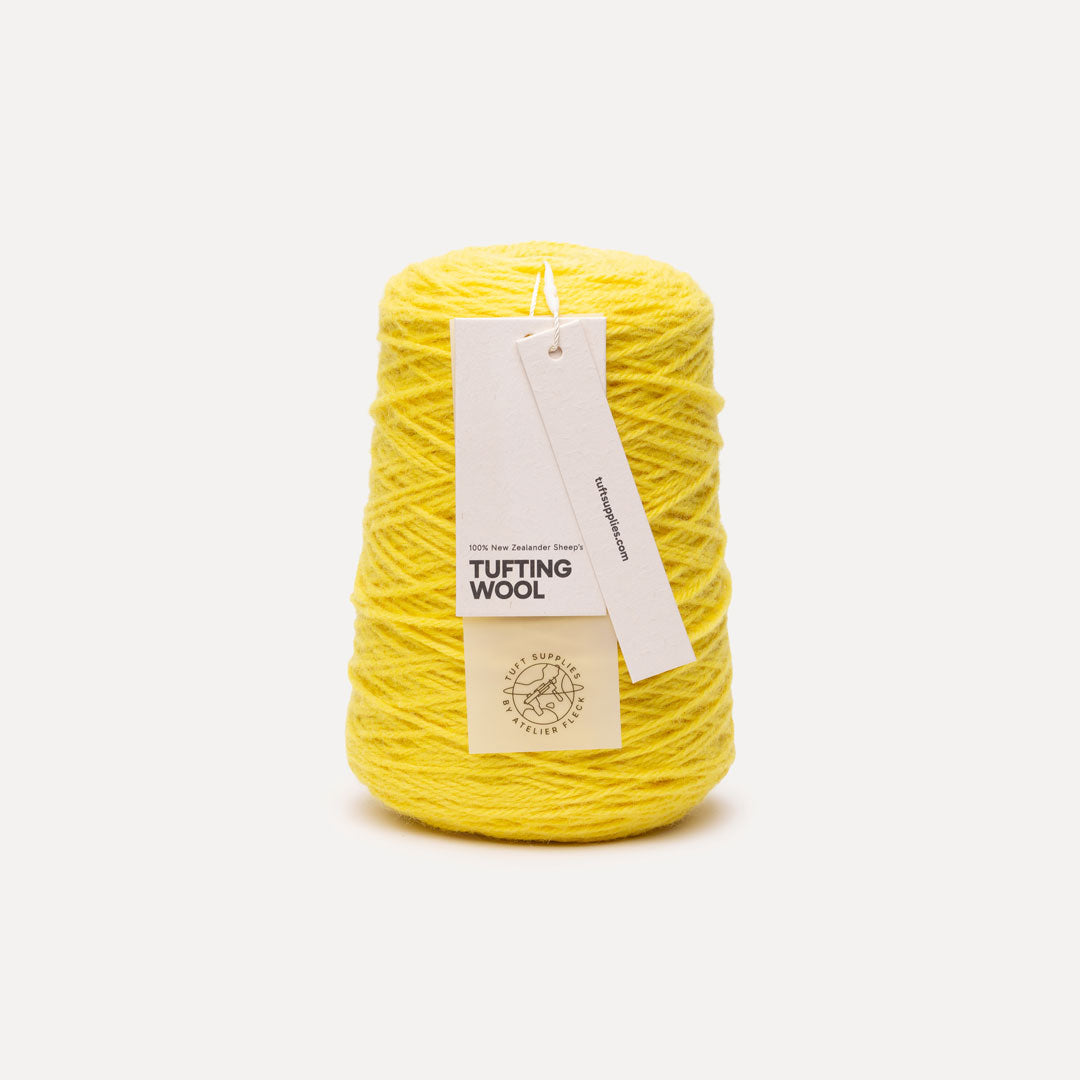 A cone of bright yellow tufting wool yarn with a white paper hangtag, set against a clean, light gray background.