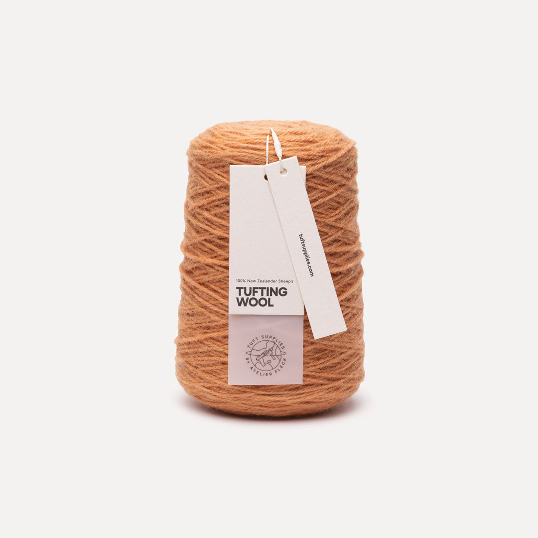 A cone of peach-colored tufting wool yarn with a white paper hangtag, set against a clean, light off-white background.