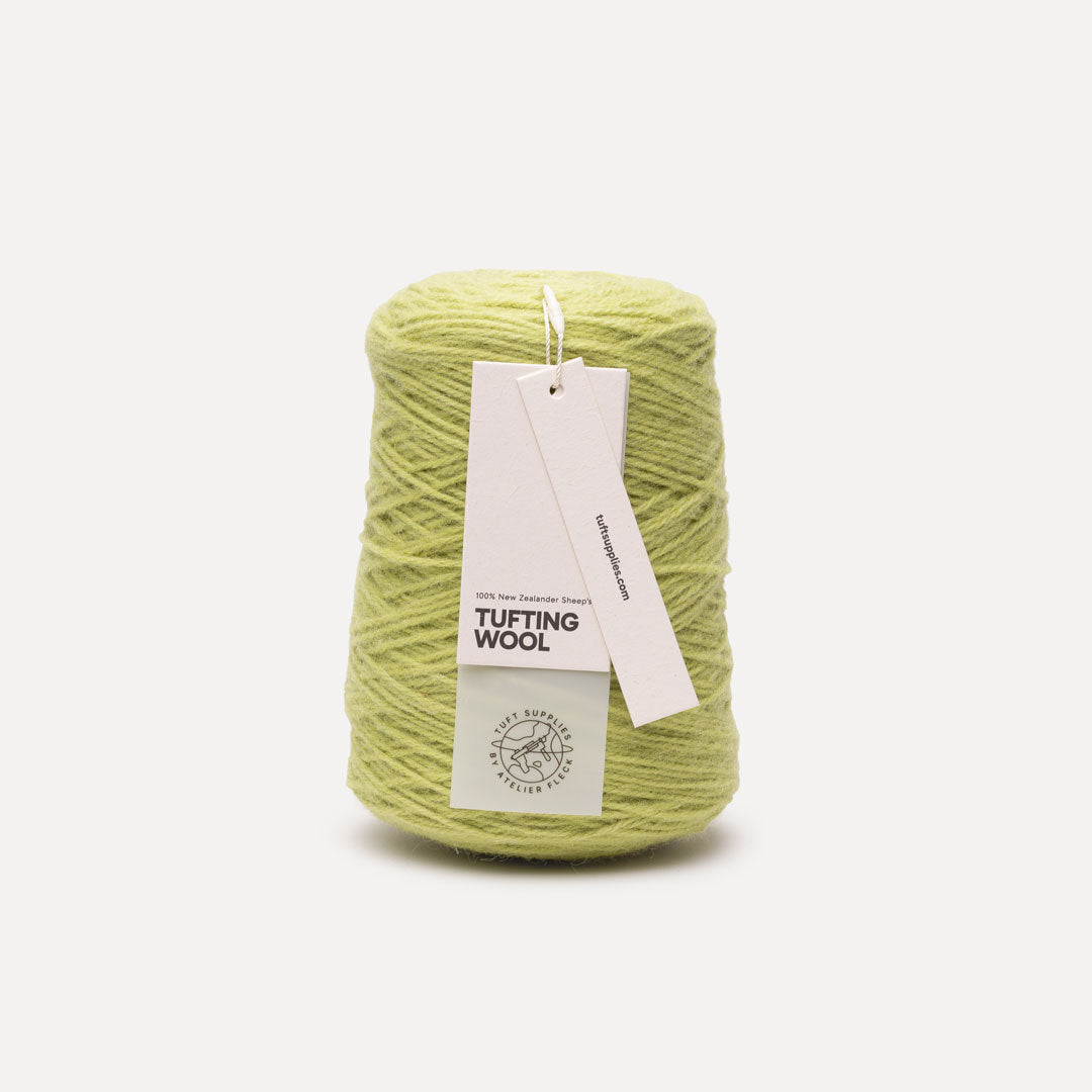 A cone of light yellow-green tufting wool yarn with a white paper hangtag, photographed on a clean white background.