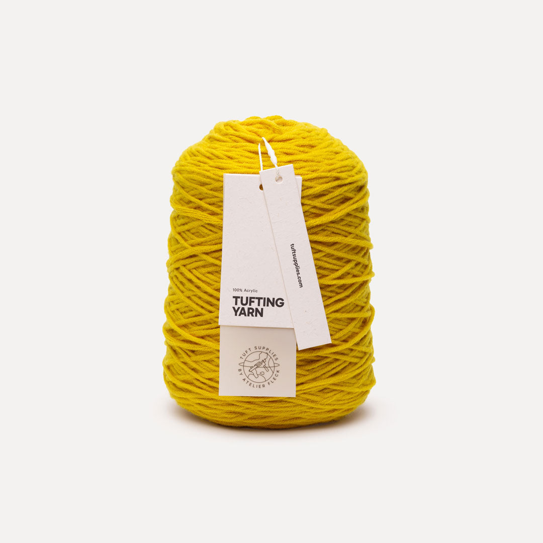 A skein of bright yellow tufting yarn with a white paper hangtag, photographed on a clean, light gray background.