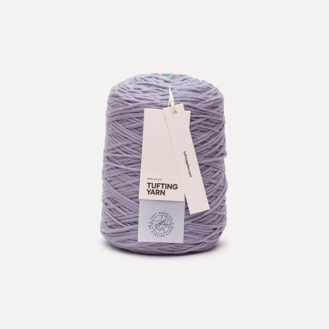 A skein of lavender-gray tufting yarn with white paper labels attached, photographed on a clean off-white background.
